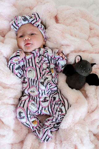 Caden Lane Ruffle Zipper Footie - Glow in the Dark Galloween
A baby wearing a pink and black witch-themed footed onesie with a matching headband, lying on a fluffy pink blanket next to a small black plush bat toy.