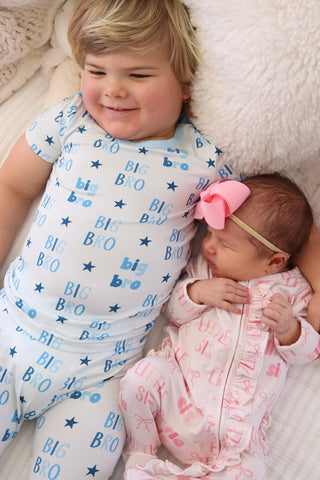 Caden Lane Ruffle Zipper Footie - Little Sis Bows
Child wearing a 'big bro' shirt lying next to a baby in pajamas on a soft surface.