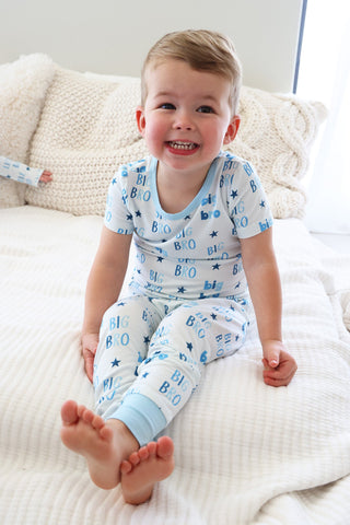 Caden Lane Two Piece Pajama Set - Big Bro Stars 
Child wearing blue pajamas with letter patterns sitting on a white bed.