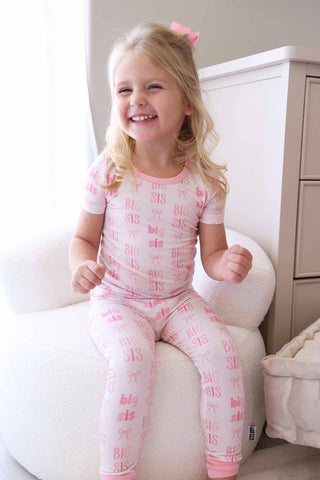 Caden Lane Two Piece Pajama Set - Big Sis Bows
Child wearing pink pajamas with 'SIS' print, sitting on a white couch.