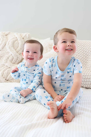 Caden Lane Zipper Footie - Little Bro Stars
Two children in matching pajamas sitting on a bed with a white background