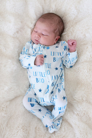 Caden Lane Zipper Footie - Little Bro Stars
Newborn baby wearing a white onesie with blue text and star patterns, lying on a soft beige surface.