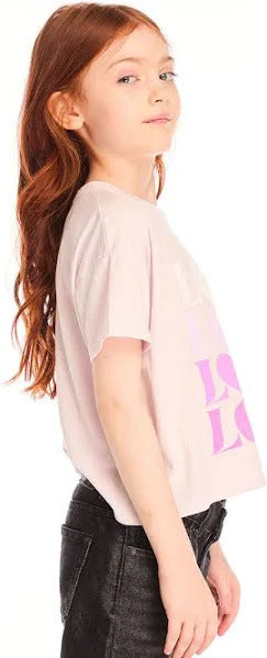 Chaser Love Tee 
Young girl wearing a light pink t-shirt with a logo on it, standing against a plain background.