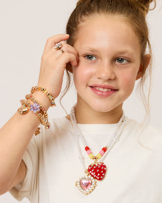 Sweetheart Surprise Lipgloss Locket
Young girl wearing colorful jewelry including a necklace with heart-shaped pendants and bracelets on a light background