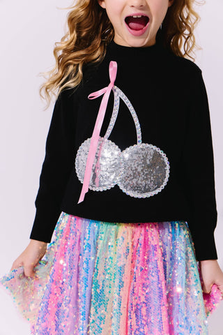 Lola and The Boys Crystal Cherry Sweater
Child wearing a black sweater with sequin cherries and a colorful skirt on a light background
