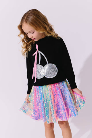 Lola and The Boys Crystal Cherry Sweater
Young girl wearing a black sweater with a silver sequin design and a colorful skirt on a white background