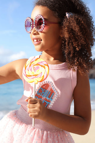 Lola and The Boys Crystal Chill Out Tank Top
Young girl in a pink dress with sunglasses and a lollipop on a beach