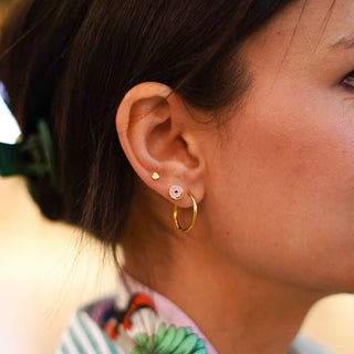Pip Pop Post Earrings - Donut Stud
Close-up of a person wearing gold hoop earrings with a blurred background