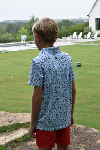 BlueQuail Clothing Co Polo Short Sleeve Shirt - Stars & Stripes
Person wearing a blue floral shirt and red shorts standing on a grassy area with a white fence in the background.