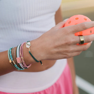 K'lani "Rally" Pickleball with Pink & Green Hair Tie Bracelets
Hand wearing multiple bracelets and a ring, holding an orange ball.