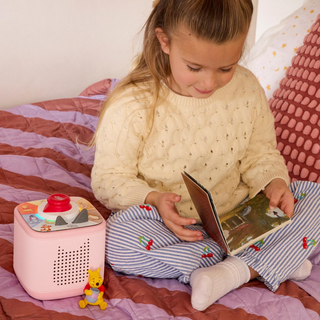 Disney Winnie the Pooh Toniebox 2 Full Play Set - Cloud Pink Young girl reading a book in bed with a pink toy beside her