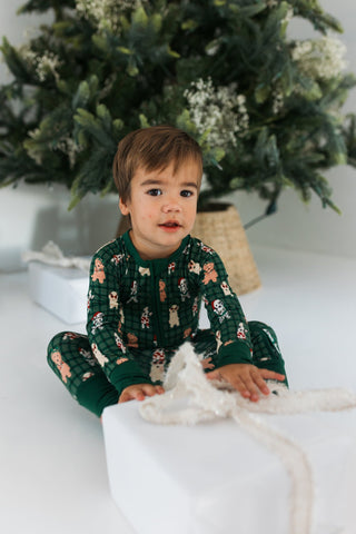 In My Jammers Christmas Pups Zipper Romper
Child wearing a green floral pajama set sitting on a white surface with a Christmas tree in the background.