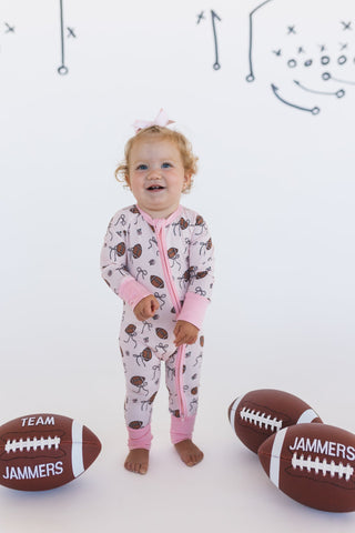 In My Jammers Blush Football Zipper Romper
Child wearing a patterned onesie with football-themed accessories on a white background