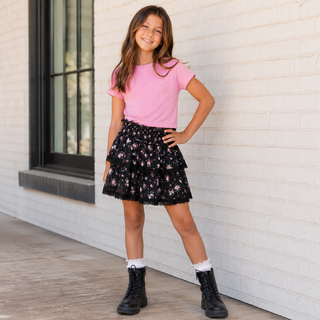 FBZ Pink Jersey Boxy Tee
A young girl stands against a white brick wall wearing a pink short-sleeve t-shirt, a black tiered ruffle skirt with a pink floral pattern, white socks, and black combat boots.
