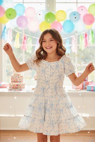 White dress by Flowers By Zoe with blue bow and heart pattern, featuring puff sleeves and a feminine, stylish design.