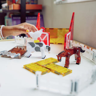 Magna-Tiles Farm™ 25-Piece Set
Toy farm set with animals and a hand interacting with a cow figure.