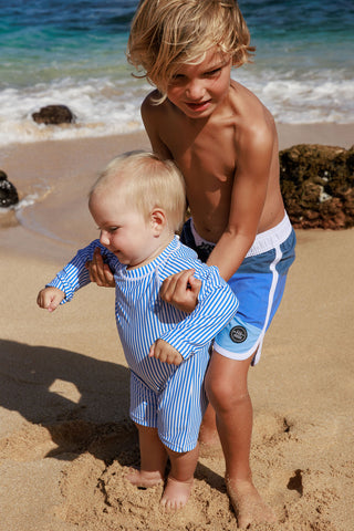 Feather 4 Arrow Cali Rashguard Surf Suit - Marina Blue
Two children on a beach, one standing and one sitting, with ocean waves in the background.