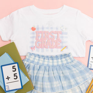 Sweet Wink First Grade Pearl Patch Short Sleeve T-Shirt
Children's outfit with 'First Grade' shirt and plaid skirt on a pink background