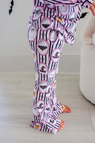 Caden Lane Girl's Two Piece Flare Lounge Set - Glow in the Dark Galloween
A child wearing a pair of Halloween-themed pajama pants with a black and white striped pattern, featuring pink witch hats, bats, ghosts, and pumpkins inside oval frames.