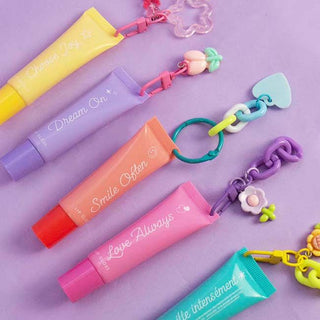 Gen Me Create Lip Gloss Charm Kit Colorful lip balm tubes with decorative keychains on a purple background
