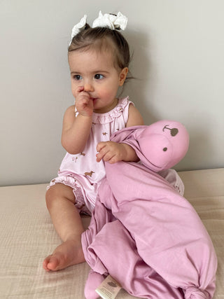 Gunamuna Bunny Lovey - Rosie
Baby in pink outfit holding a pink toy on a light-colored surface