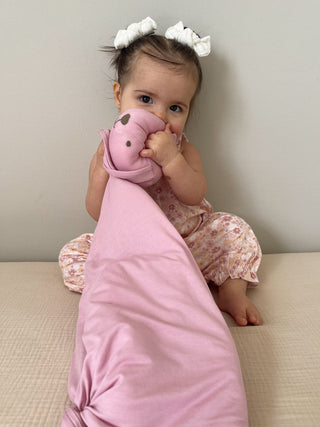 Gunamuna Bunny Lovey - Rosie
Baby wrapped in a pink blanket and holding a pink toy, sitting on a light-colored surface.