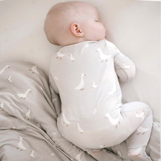 Gunamuna Convertible Romper Footie - Goose
Baby in a white onesie with duck pattern lying on a matching blanket.