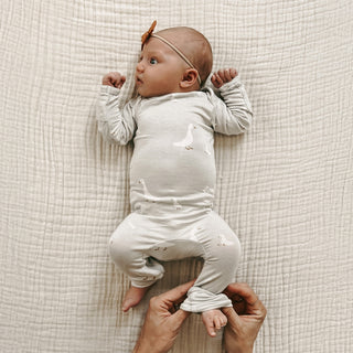 Gunamuna Convertible Romper Footie - Goose
Baby in a light gray onesie lying on a textured beige blanket