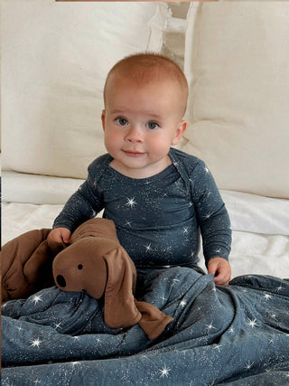 Gunamuna Pup Lovey - Peanut
A baby sitting on a white bed wearing a dark blue long-sleeve bodysuit and matching blanket with a white starry pattern, holding a brown plush dog toy.