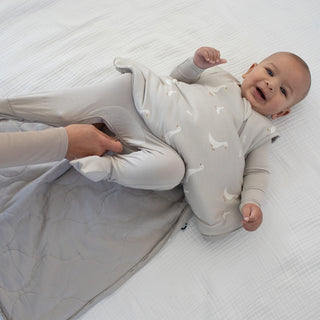 Gunamuna Sleep Sack 1.0 TOG - Goose
Baby in a light gray sleep suit with subtle pattern lying on a white textured surface.