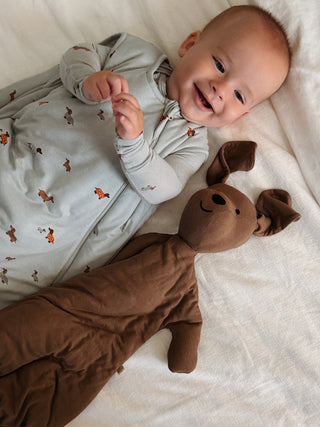 Gunamuna Sleep Sack 1.0 TOG - Woof
Baby lying on a white blanket with a brown plush toy