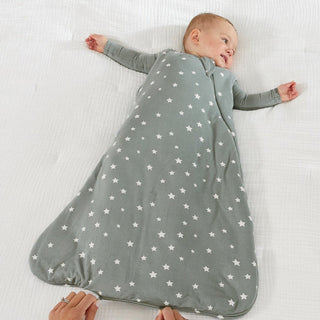 Gunamuna Sleep Sack 2.5 TOG - Shine
A baby lying on a white textured blanket, wearing a gray sleep sack with a white star pattern. Hands are visible at the bottom adjusting the sleep sack.