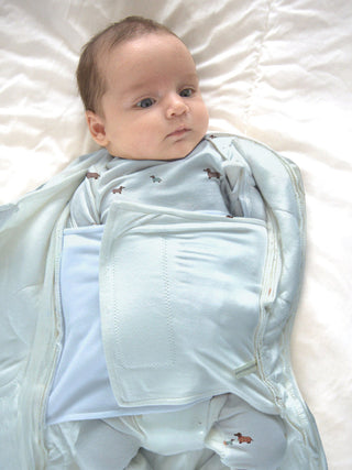 Gunamuna Swaddle Sleep Sack 1.0 TOG - Woof 
Baby wrapped in a light blue swaddle on a white blanket