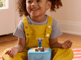 Tonies Character - The Laurie Berkner Band: Harry the Chipmunk's Treasure Hunt
Child wearing yellow overalls with a blue toy on a wooden floor