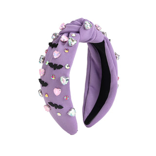 Sweet Wink Bat Halloween Gemstone Headband
A lavender purple fabric headband featuring a knotted top detail, decorated with various embellishments including pink and silver heart-shaped rhinestones, black bat silhouettes, and small colorful charms, shown against a plain white background.