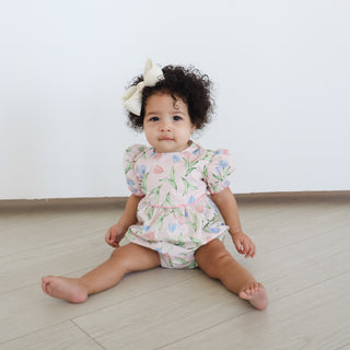 Hollis Baker Everly Bubble - Tulips
Baby sitting on a light wooden floor wearing a floral romper.
