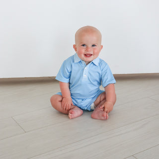 Hollis Baker Tripp Romper - Blue Stripe
Baby sitting on a light wooden floor wearing a blue striped shirt and diaper.
