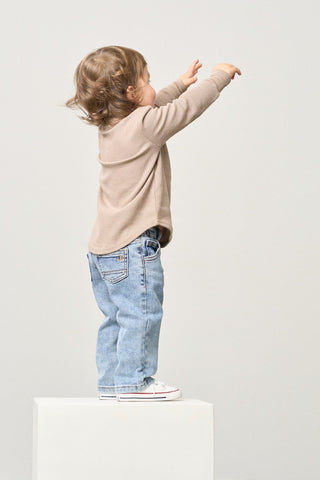 Little Bipsy Straight Leg Jean - Light Wash
Child standing on a white pedestal wearing a beige sweater and blue jeans against a plain background