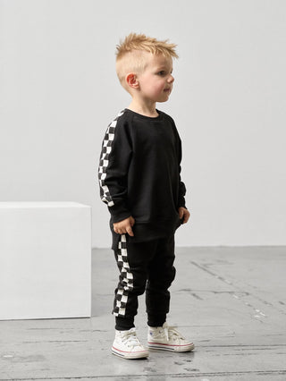 Little Bipsy Stripe Checkered Jogger - Black
Child wearing a black outfit with checkered patterns on a light gray background