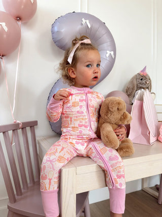 In My Jammers Zipper Romper - Birthday Girl
Child in pink pajamas holding a teddy bear, surrounded by balloons and a balloon animal.