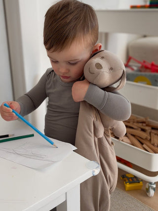 Gunamuna Pup Lovey - Mutts
Child holding a plush toy and drawing with a blue pen on a white surface.