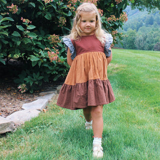 Pink Chicken Girls Kit Dress - Mixed Checks
Young girl in a layered dress standing in a grassy area with greenery.