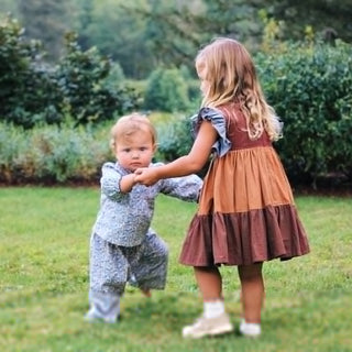 Pink Chicken Girls Kit Dress - Mixed Checks
Two children holding hands in a grassy outdoor setting