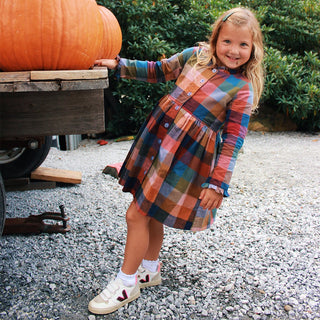 Pink Chicken Girls Autumn Dress - Harvest Check
Child in a plaid dress standing next to a pumpkin on a gravel surface with greenery in the background
