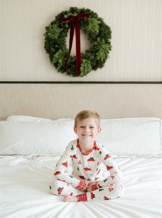 In My Jammers Red Holly Jolly Cruisers Two Piece Set
Child in pajamas sitting on a bed with a Christmas wreath on the wall.