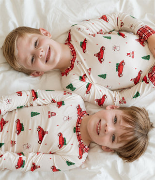 In My Jammers Red Holly Jolly Cruisers Two Piece Set
Two children wearing pajamas with Christmas patterns lying on a white surface.