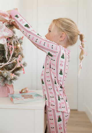 In My Jammers Pinkmas Two Piece Set 
Child in festive pajamas decorating a small Christmas tree.