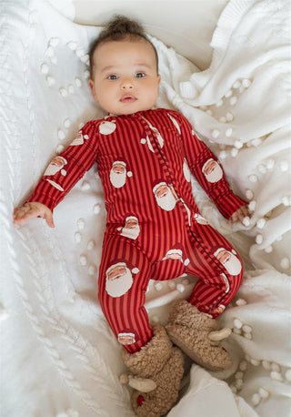 In My Jammers Santa Zipper Romper
Baby wearing red Santa Claus pajamas lying on a white blanket with a small brown plush toy.