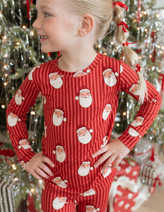 In My Jammers Santa Two Piece Set
Child wearing a red Santa Claus pajama set in front of a Christmas tree.
