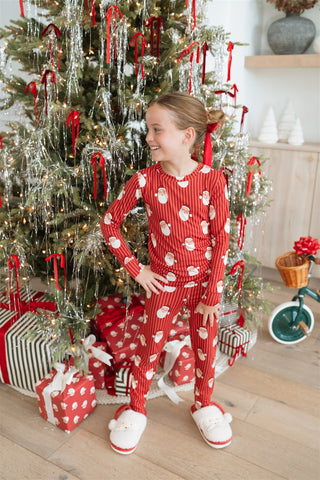 In My Jammers Santa Two Piece Set
Child in red pajamas with white polka dots standing in front of a decorated Christmas tree.